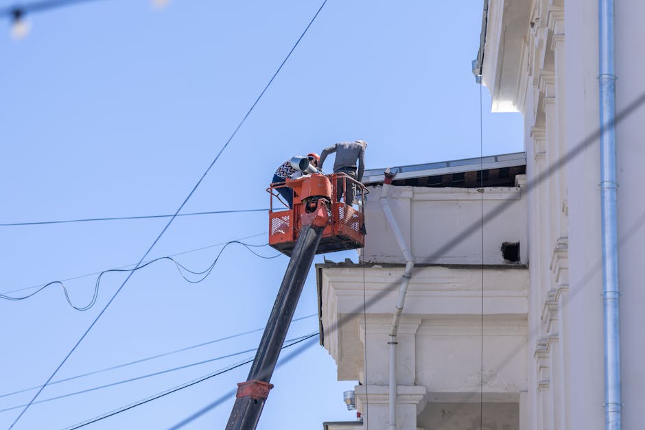 Workers on lift repairing building façade under clear sky.